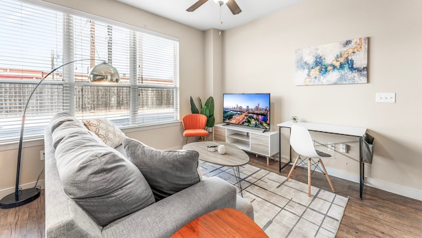 A modern living room with a sofa, a TV, a desk, and a ceiling fan. - Cozy Soco 1BR King Suite w Gympickleballlaundry (Austin)