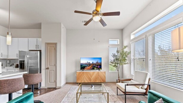 A modern living room with teal sofas, a coffee table, a TV, and a ceiling fan. - Elegant 2BR King Suite Fast Wifi 8 min to DT (Austin)