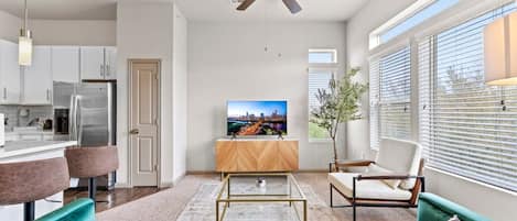 Una sala moderna con sofás azul verdoso, una mesa de centro, un televisor y un ventilador de techo.