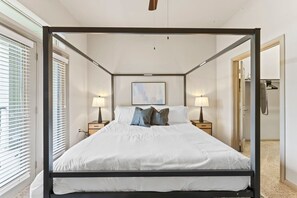 A four-poster bed with white bedding, two bedside tables with lamps, a framed picture on the wall, and a door to the right. - Elegant 2BR King Suite Fast Wifi 8 min to DT (Austin)