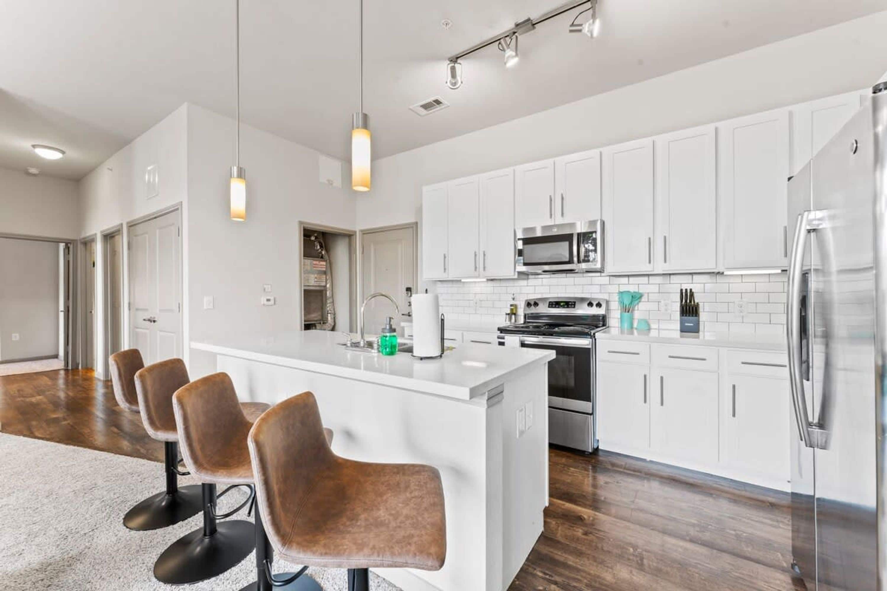 A modern kitchen with white cabinets, stainless steel appliances, and a central island with bar stools.