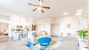 A modern living room with a blue chair, a sofa, and a dining area with a table and chairs. - Spacious 2BR King Beds Suite 8 Min to Downtown (Austin)