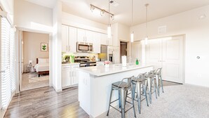A modern kitchen with white cabinetry, stainless steel appliances, and a central island with bar stools. - Spacious 2BR King Beds Suite 8 Min to Downtown (Austin)