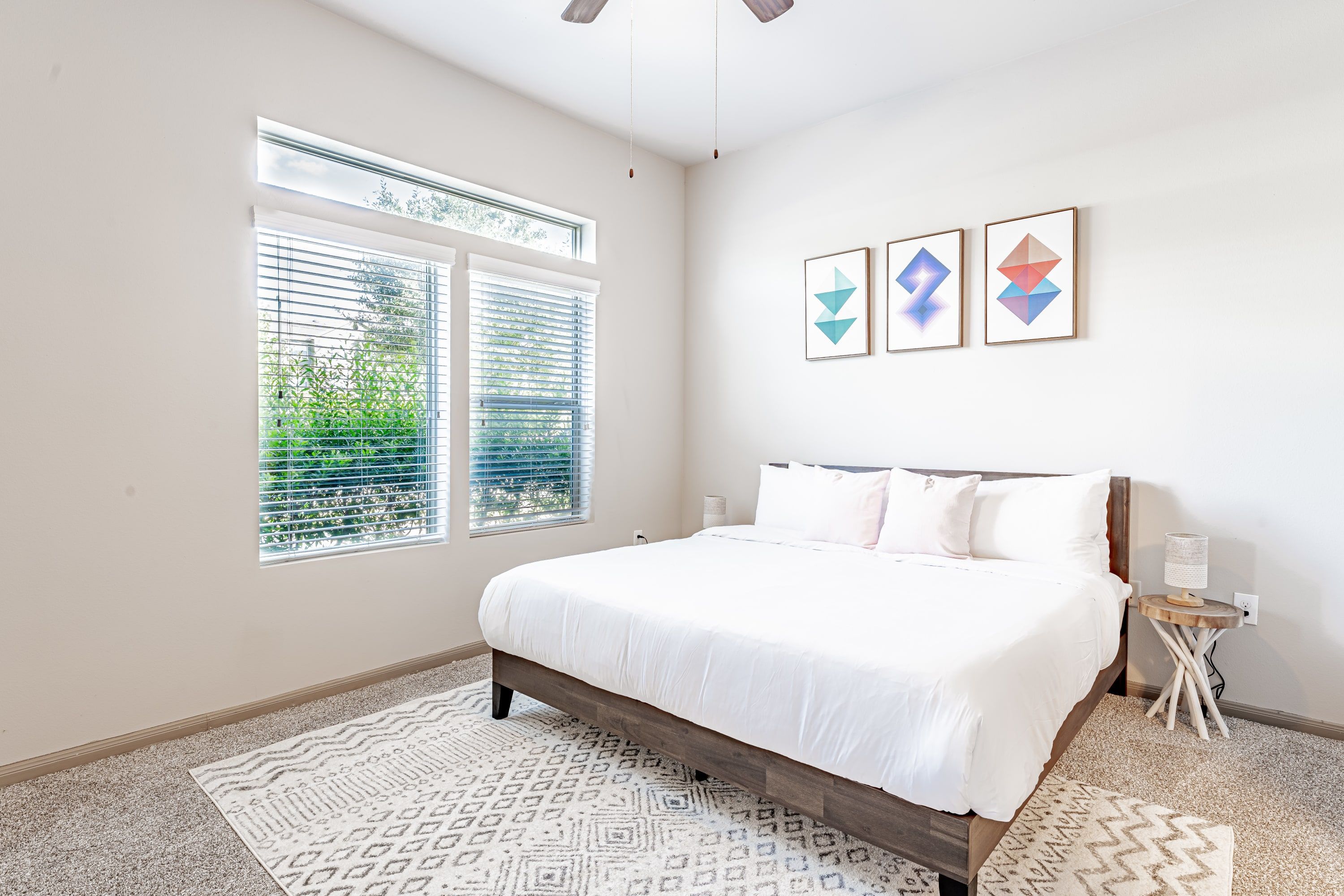 Un dormitorio con cama, ventana con persianas, mesita de noche y decoración en la pared.