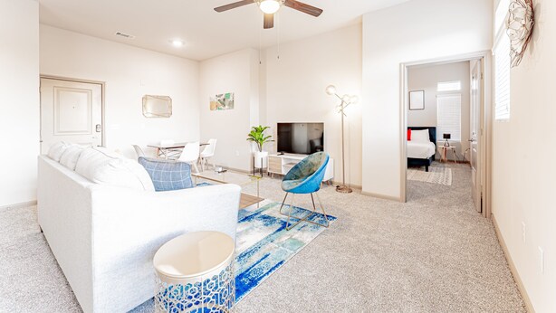 A modern living room with a white sofa, a blue chair, a TV, and a ceiling fan. - Spacious 2BR King Beds Suite 8 Min to Downtown (Austin)