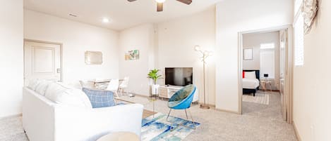 Una sala de estar moderna con un sofá blanco, un sillón azul, un televisor y un ventilador de techo.