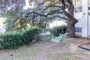 A swing set under a large tree in a landscaped area with a building in the background. - Soco Chic 1BR w Pool King bed Close to DT (Austin)
