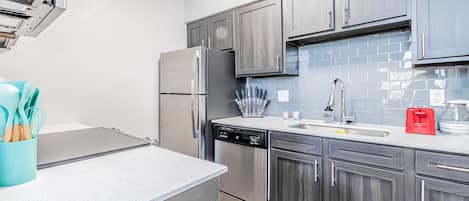 A modern kitchen with stainless steel appliances, grey cabinetry, and a tiled backsplash.