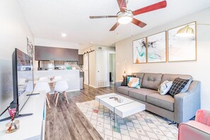 A modern living room with a grey sofa, white coffee table, and a ceiling fan. - Soco Chic 1BR w Pool King bed Close to DT (Austin)