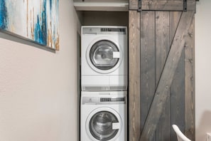 A laundry room with two stacked front-loading washing machines, a wooden door, and a painting on the wall. - Trendy Soco 1BR Suite King bed Fast Wifi w Pool (Austin)