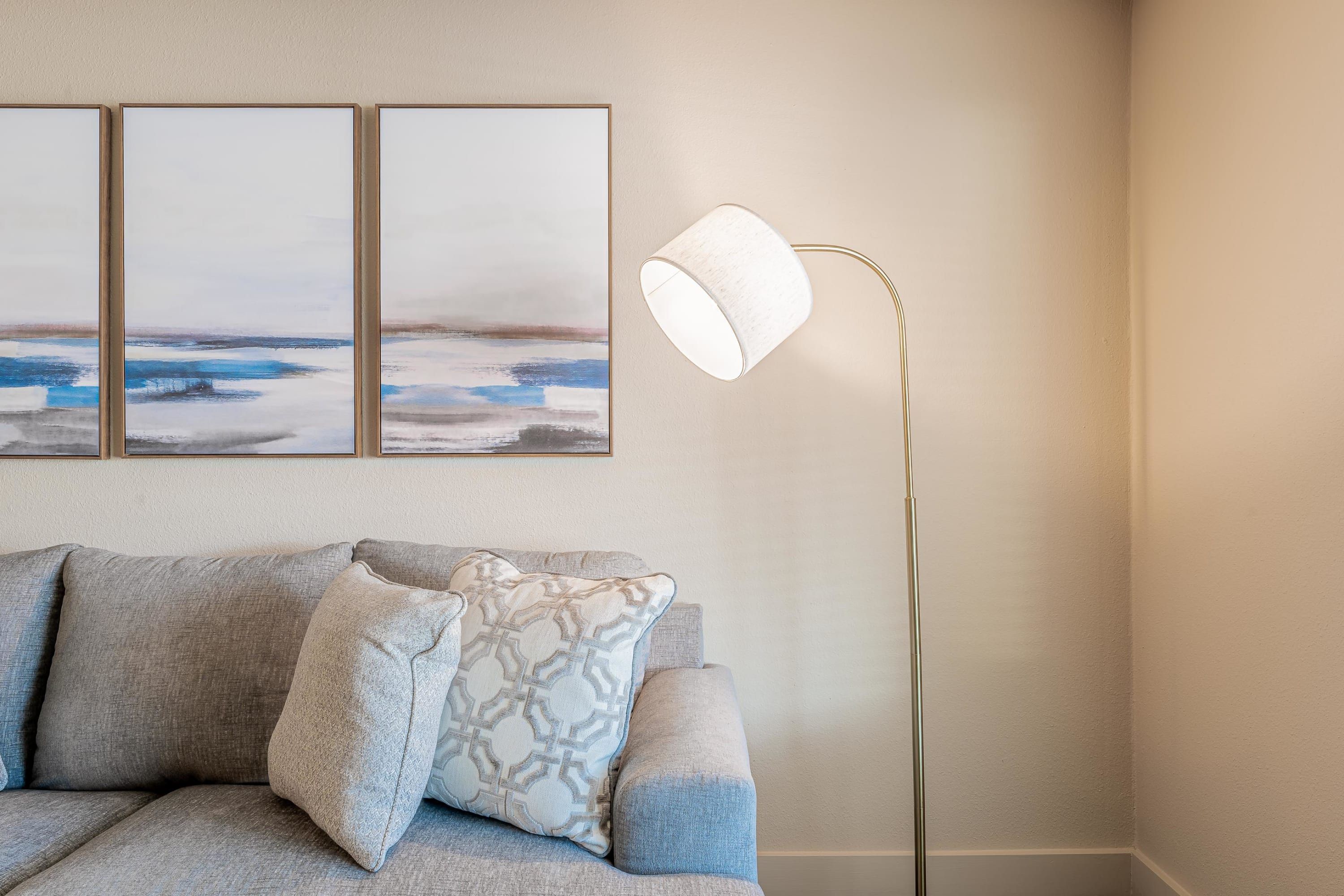 Een kamer met een bank, een vloerlamp en drie ingelijste kunstwerken aan de muur.