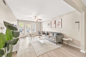 A spacious living room with a sofa, coffee table, and a large plant. - Quaint 2BR King Suite w Gym Close to DT (Austin)