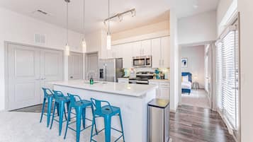 Een moderne keuken met witte kasten, roestvrijstalen apparatuur en een centraal keukenblok met barstoelen.