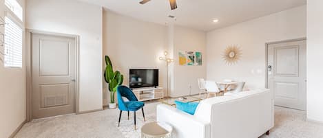 Una sala de estar moderna con un sofá blanco, un sillón azul, una mesa de centro y un ventilador de techo.