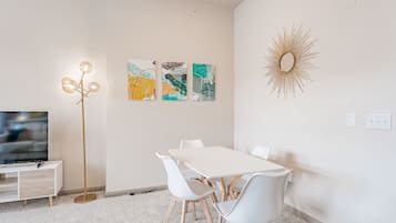 A modern living room with a white table, white chairs, a floor lamp, and abstract wall art.