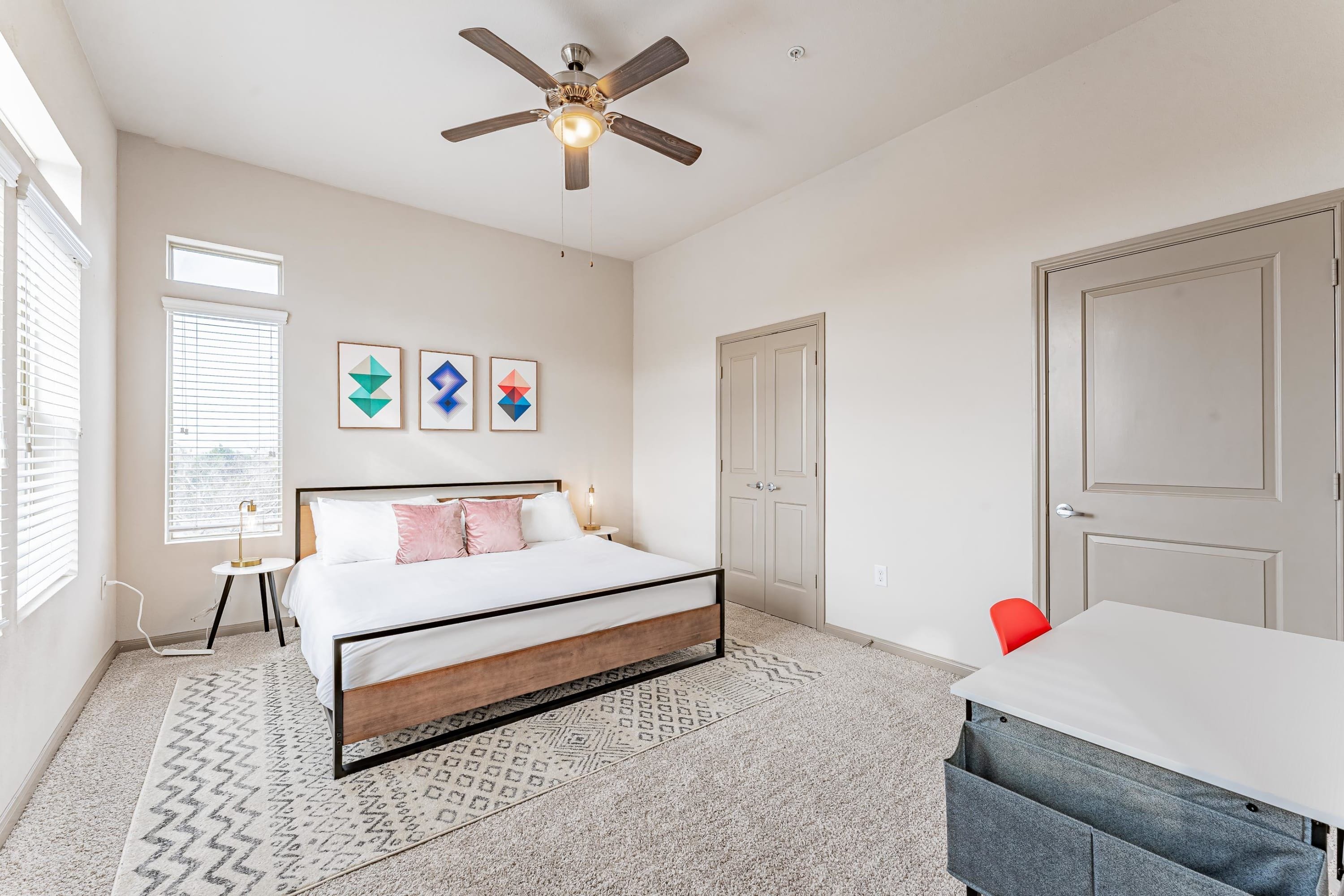 A bedroom with a bed, a ceiling fan, a desk, and a chair.