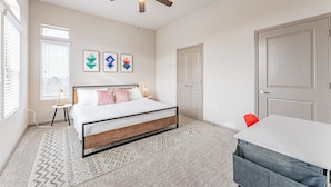 Um quarto com cama, ventilador de teto, escrivaninha e cadeira.