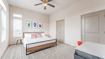 A bedroom with a bed, a ceiling fan, a desk, and a chair.