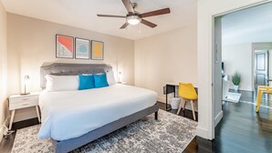 A bedroom with a bed, a ceiling fan, a nightstand, a desk, a chair, and a potted plant. - Peaceful 2BR King Beds Suite Next to DT w Pool (Austin)