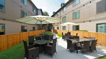 An outdoor patio area with tables and chairs, surrounded by a wooden fence and a building with multiple windows.