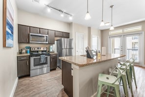 A modern kitchen with stainless steel appliances, a granite countertop, and a bar area with stools. - Trendy Soco 2BR King Suite w Gympickleballlaundry (Austin)
