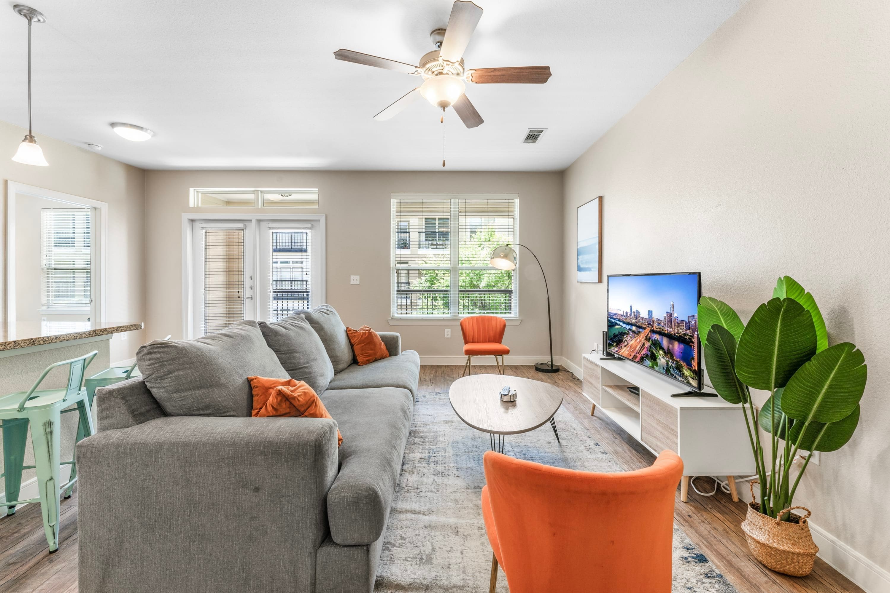 A modern living room with a grey sofa, orange armchair, and a flat-screen TV.