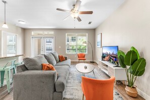 A modern living room with a grey sofa, orange armchair, and a flat-screen TV. - Trendy Soco 2BR King Suite w Gympickleballlaundry (Austin)