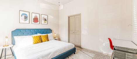 Habitación de hotel con cama, ventilador de techo, una puerta y una mesita con lámpara.