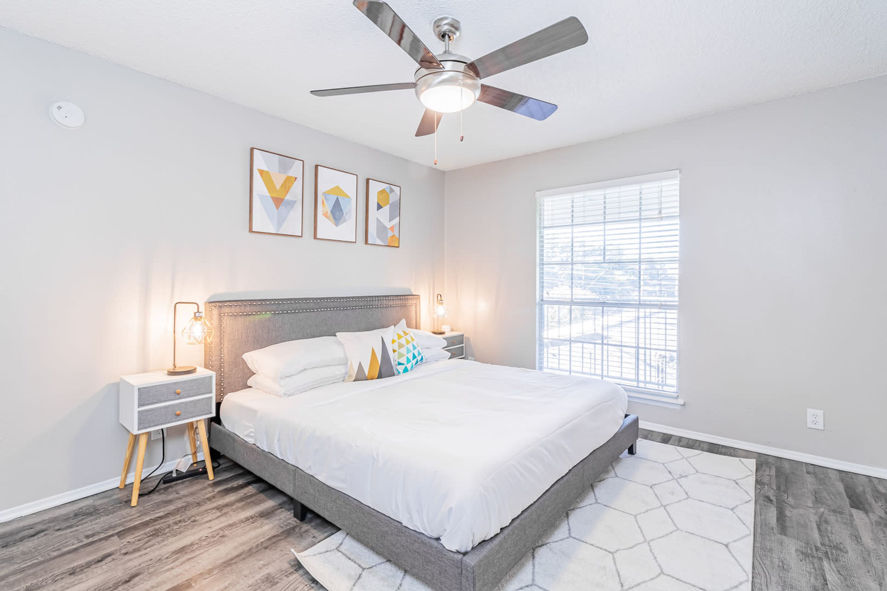 A bedroom with a bed, nightstands, a ceiling fan, and a window.