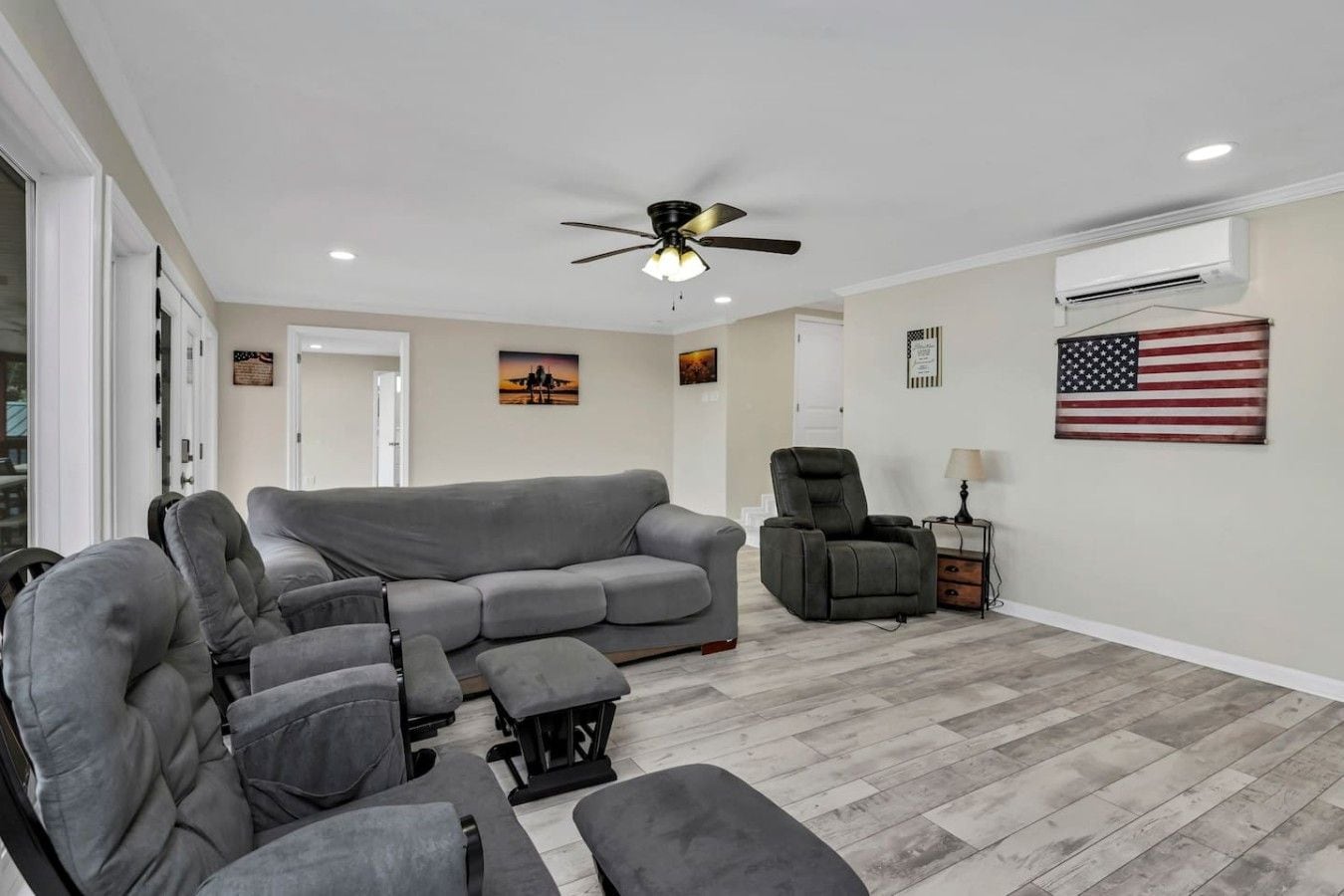 Een woonkamer met een grijze hoekbank, een fauteuil, een plafondventilator en een Amerikaanse vlag aan de muur.