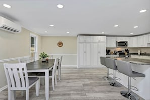 A modern kitchen with white cabinetry, a central island with bar stools, and a dining area with a table and chairs.