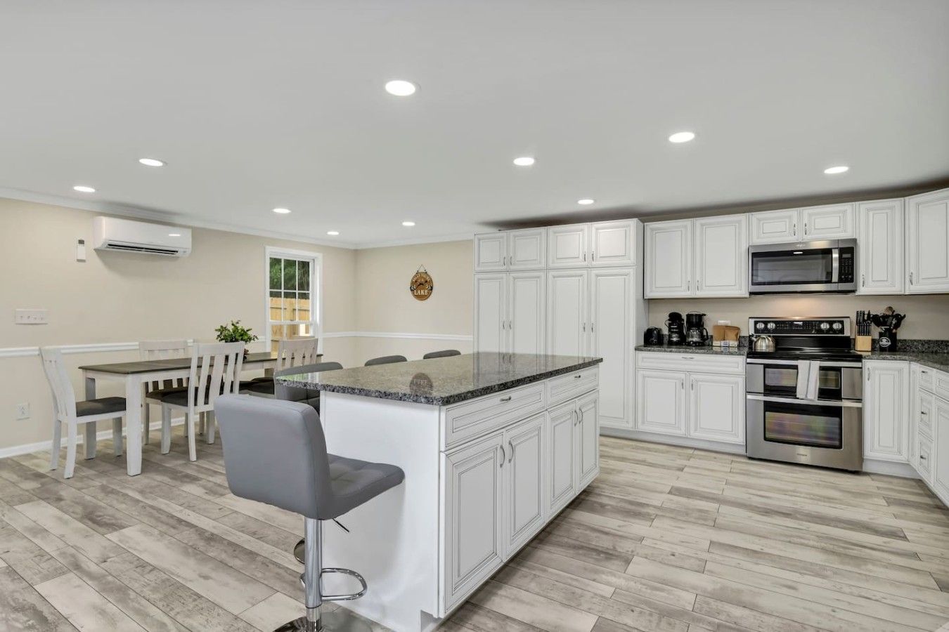 A kitchen with white cabinetry, a granite countertop island, stainless steel appliances, and a dining area with a table and chairs.