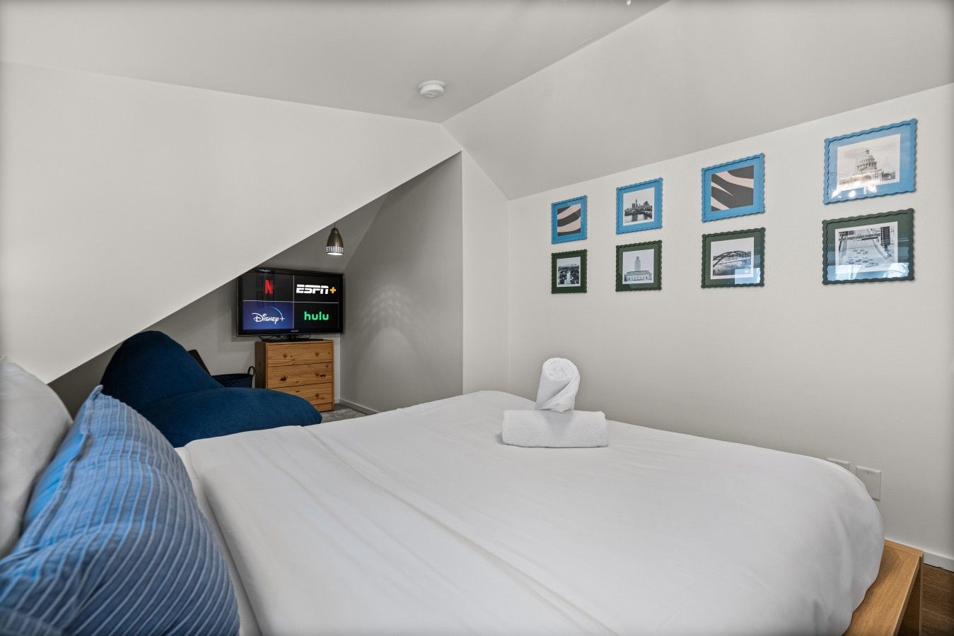 Ein Schlafzimmer mit einem Bett, einem Fernseher, der Streaming-Dienste anzeigt, und gerahmten Bildern an der Wand.