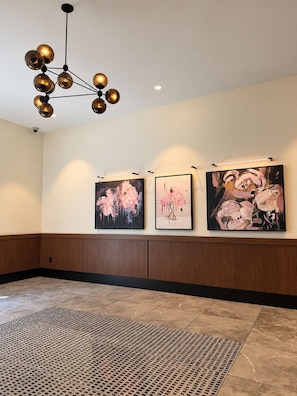 A hallway with three framed artworks on the wall, a patterned rug on the floor, and a modern chandelier. - The Westside Retreat 2BD|2BTH (Atlanta)