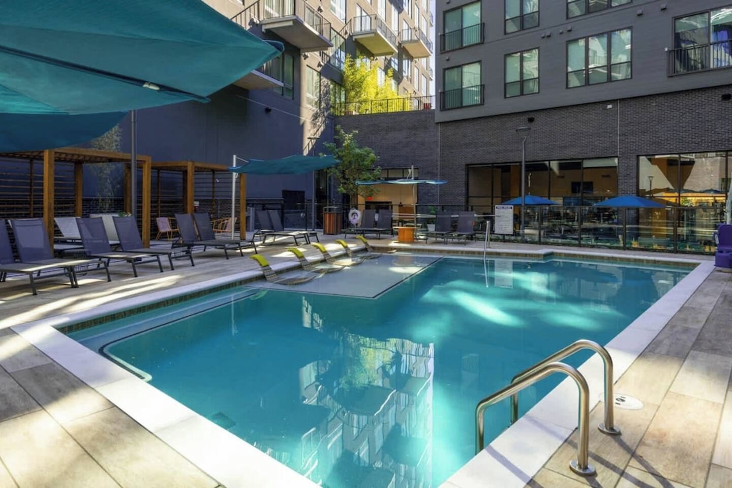 Une piscine dotée de chaises longues et de parasols, entourée d’un bâtiment avec des balcons.