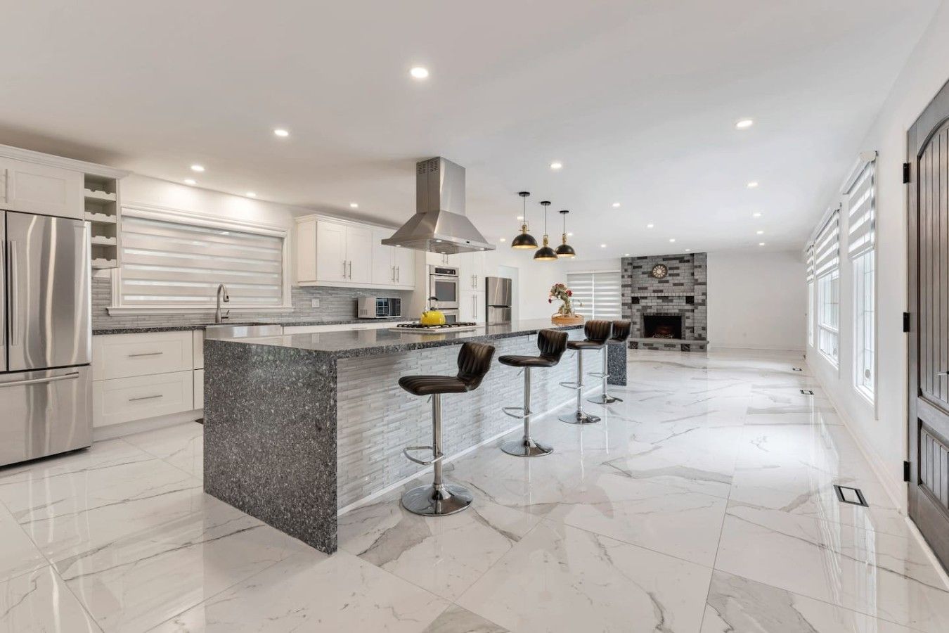A modern kitchen with a central island, bar stools, stainless steel appliances, and a fireplace.
