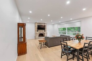 Una sala moderna con chimenea, un televisor grande, un sofá y una zona de comedor con una mesa y sillas de madera.