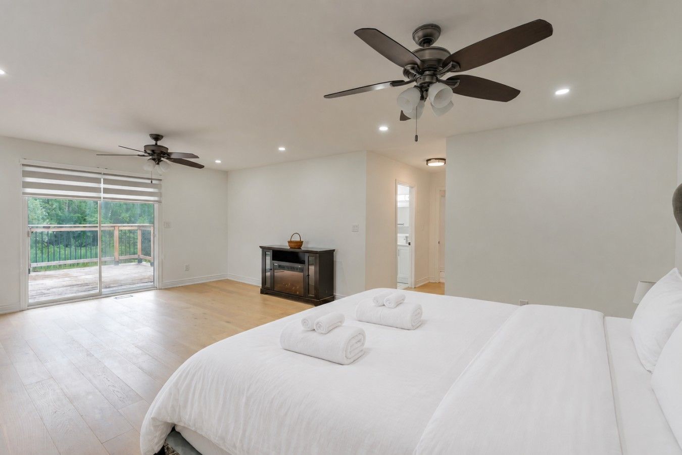 A bedroom with a large bed, two ceiling fans, a sliding glass door to a balcony, and a small table with a basket.