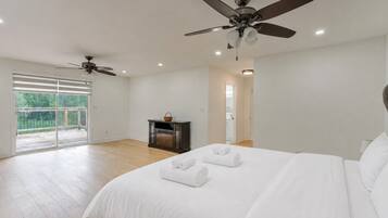 A bedroom with a large bed, two ceiling fans, a sliding glass door to a balcony, and a small table with a basket.