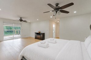 Un dormitorio con una cama grande, dos ventiladores de techo, un puertas corredera de cristal a un balcón y una pequeña mesa con una cesta.