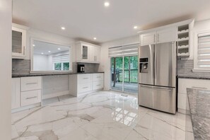 A modern kitchen with white cabinetry, a stainless steel refrigerator, and a marble floor.