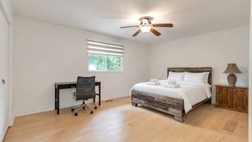 A bedroom with a bed, a desk, a chair, a ceiling fan, and a window.
