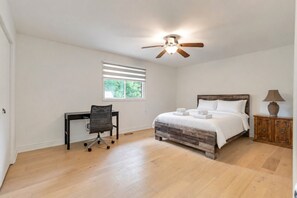 Un dormitorio con cama, escritorio, silla, ventilador de techo y ventana.