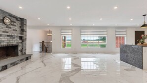 A spacious living room with a fireplace, large windows, and a marble floor.