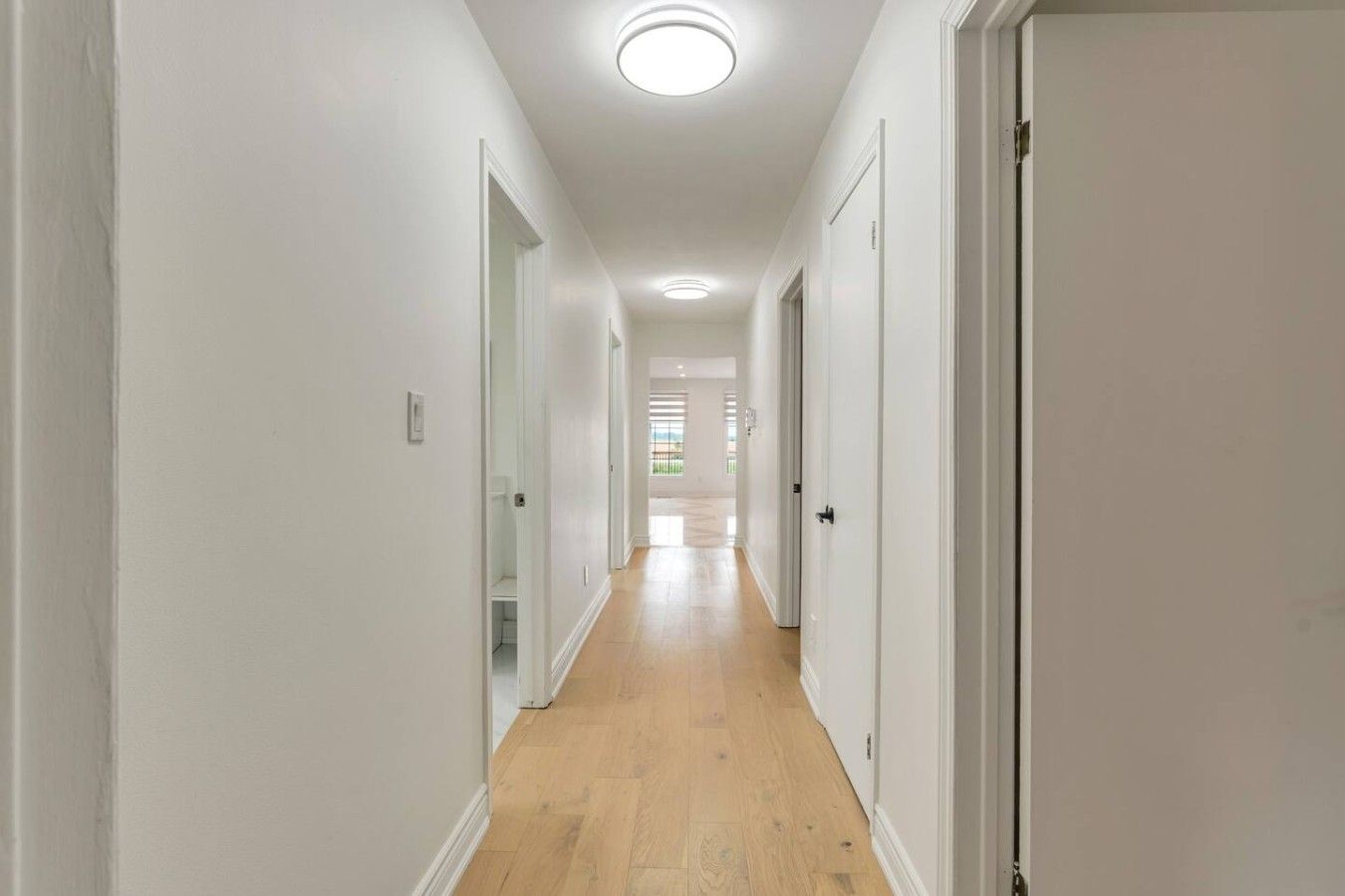 A hallway with white walls, wooden flooring, and doors leading to other rooms.