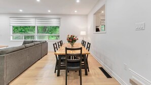 A dining area with a wooden table, chairs, a sofa, and a window with blinds.