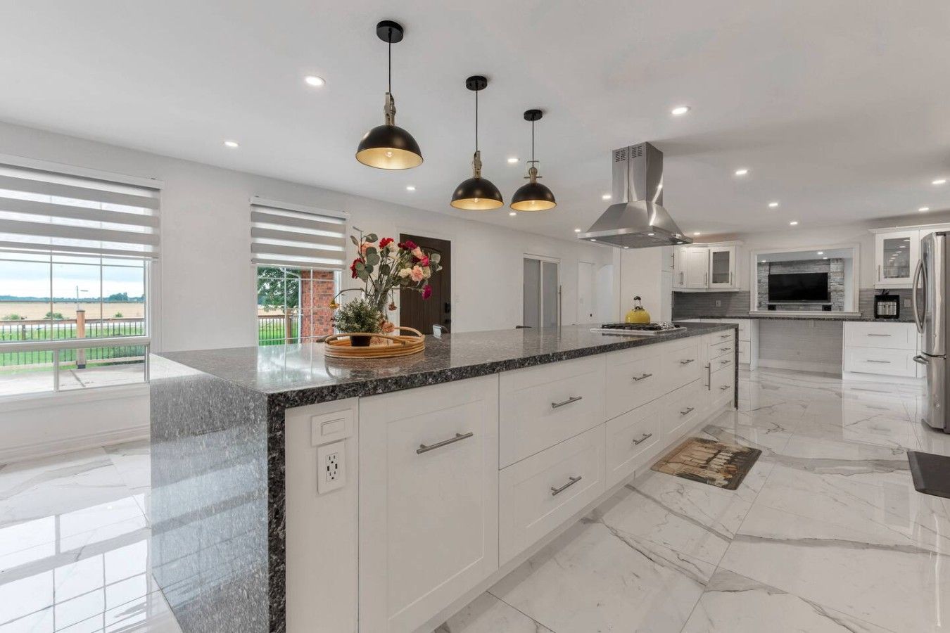A modern kitchen with a marble countertop, white cabinetry, and pendant lighting.