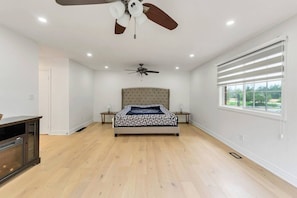 A bedroom with a bed, two nightstands, a ceiling fan, a window with blinds, and a door.