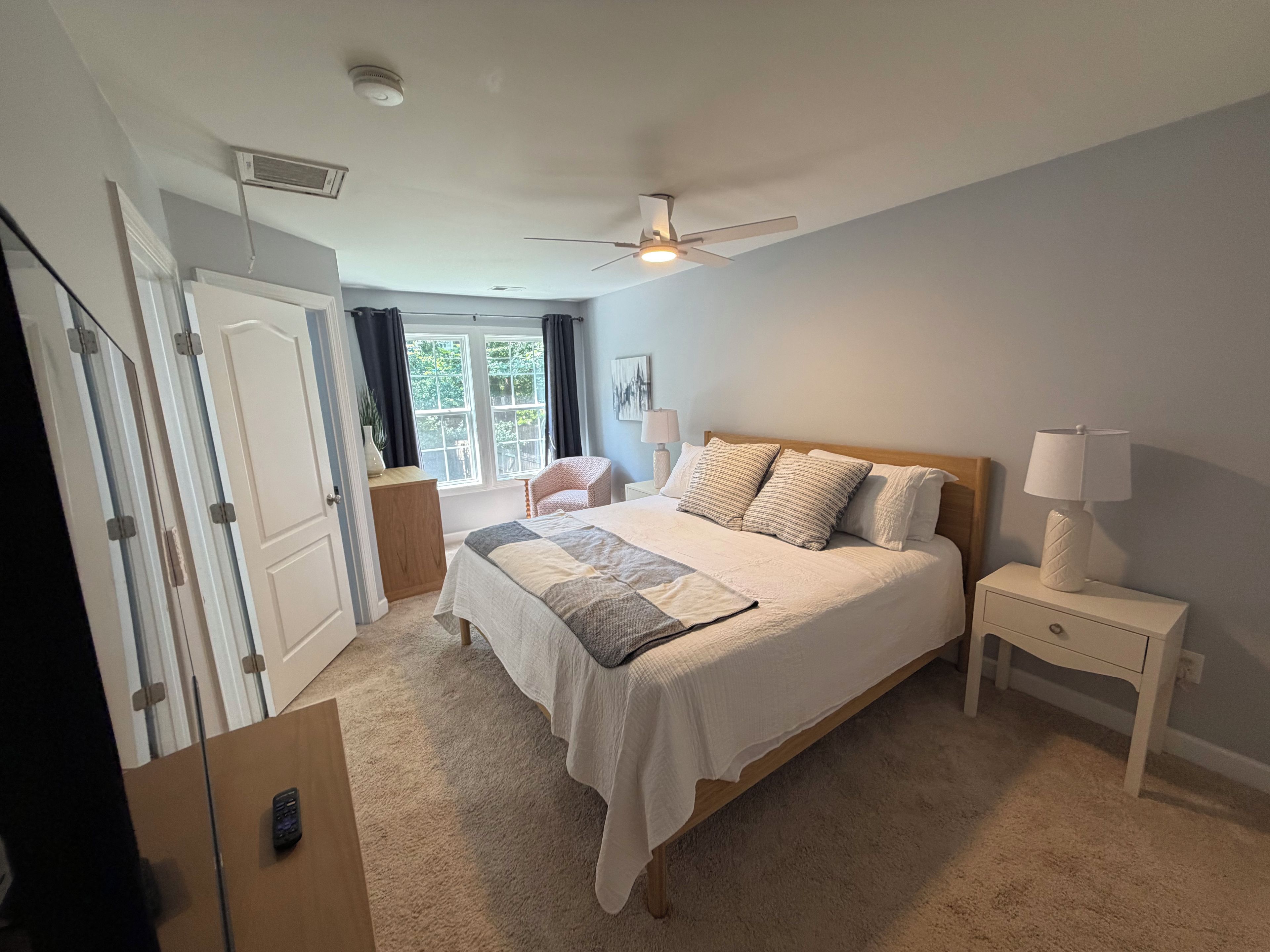 A bedroom with a bed, bedside table, lamp, and a view of the outdoors.