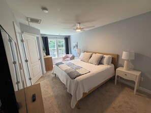 A bedroom with a bed, bedside table, lamp, and a view of the outdoors.